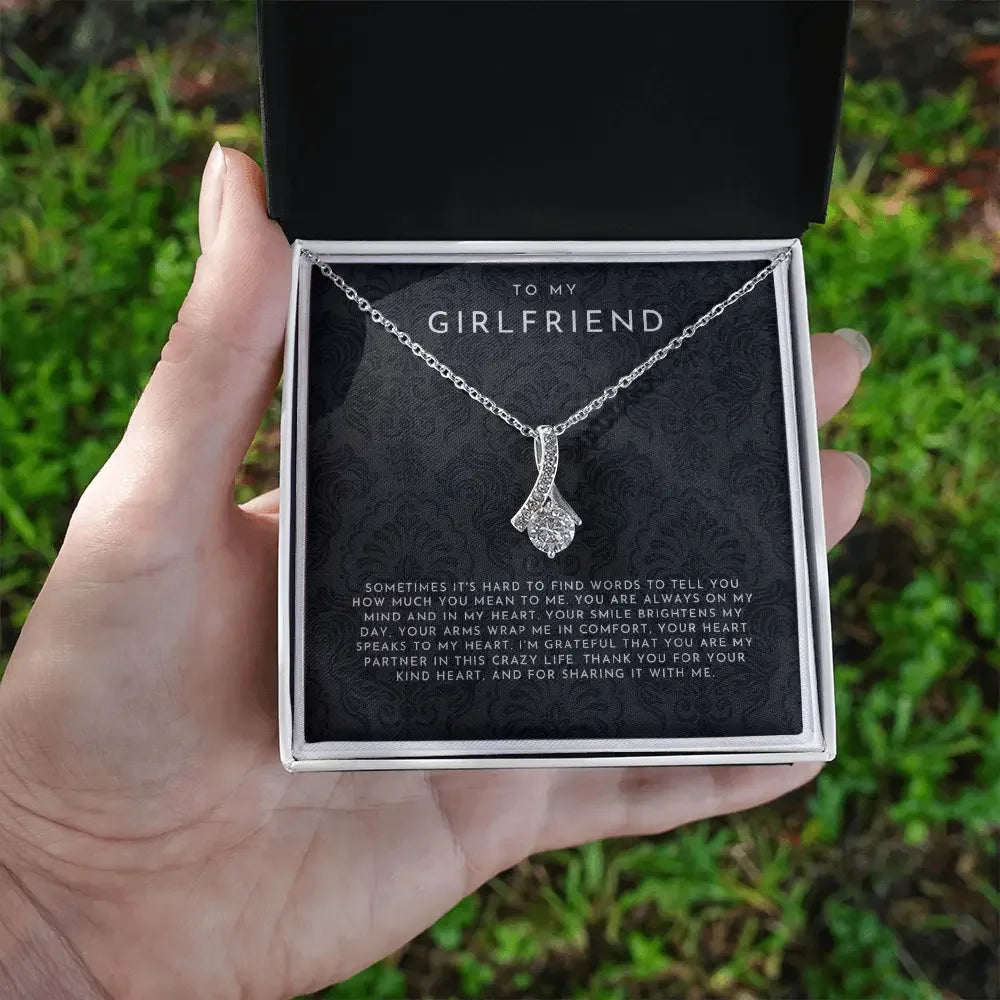Hand holding gift box with silver pendant necklace and heartfelt message to girlfriend}